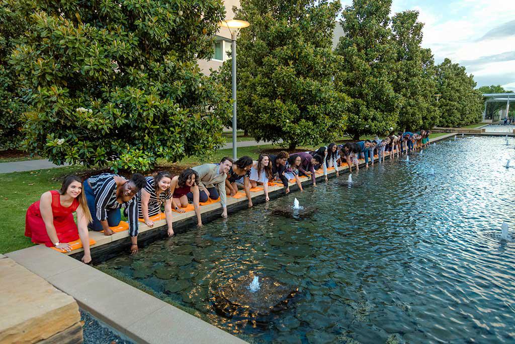 戒指的传统. 照片中，人们跪在校园倒影池边，用手泡水.