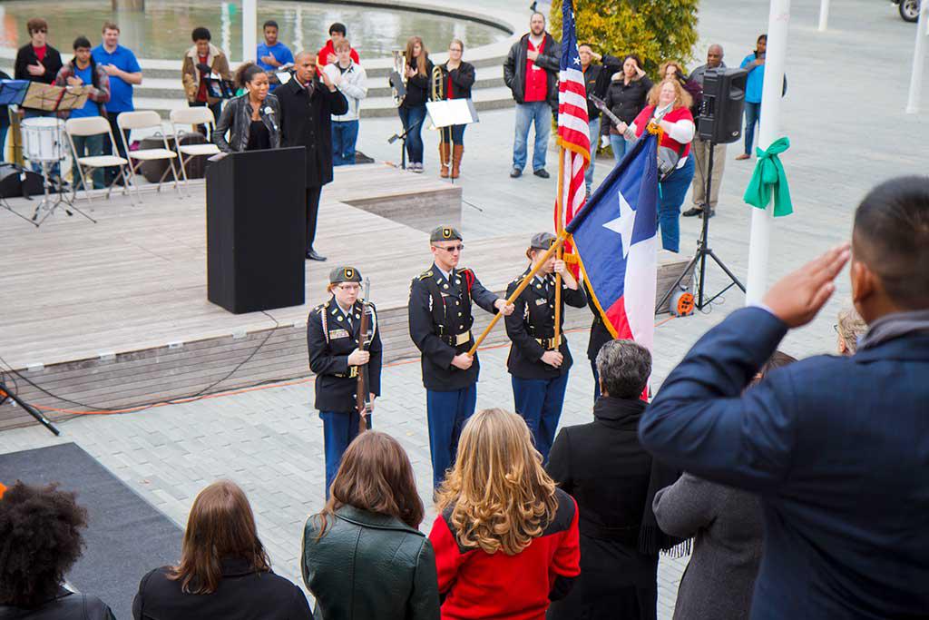 支持退伍军人. 图为三名身穿军装的人在基座上展示国旗.